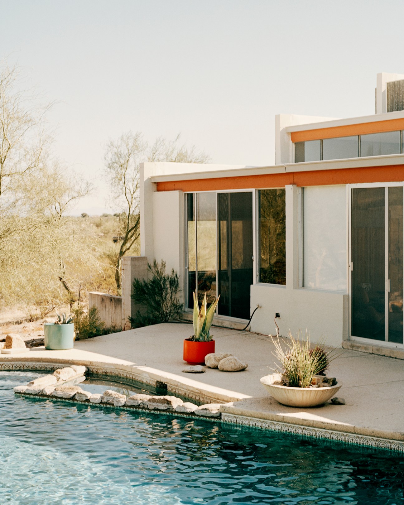 Modern desert house pool area with concrete patio, planters, and glass walls overlooking arid landscape