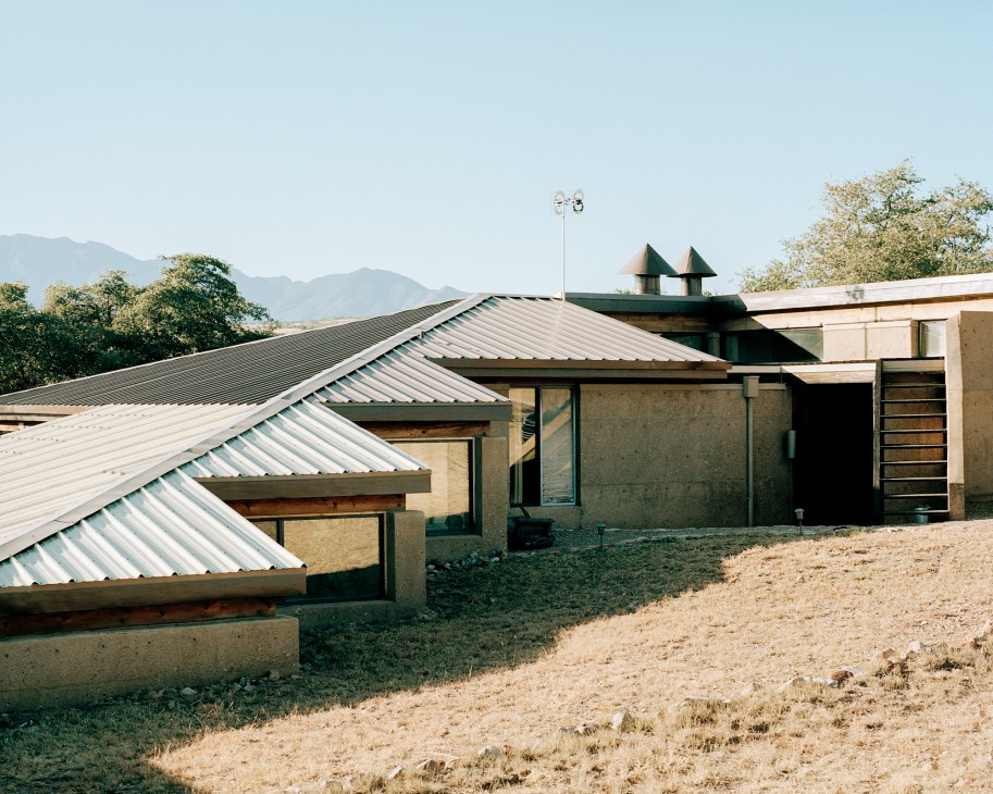 Modern desert house with corrugated metal roofing and concrete walls set against mountainous landscape