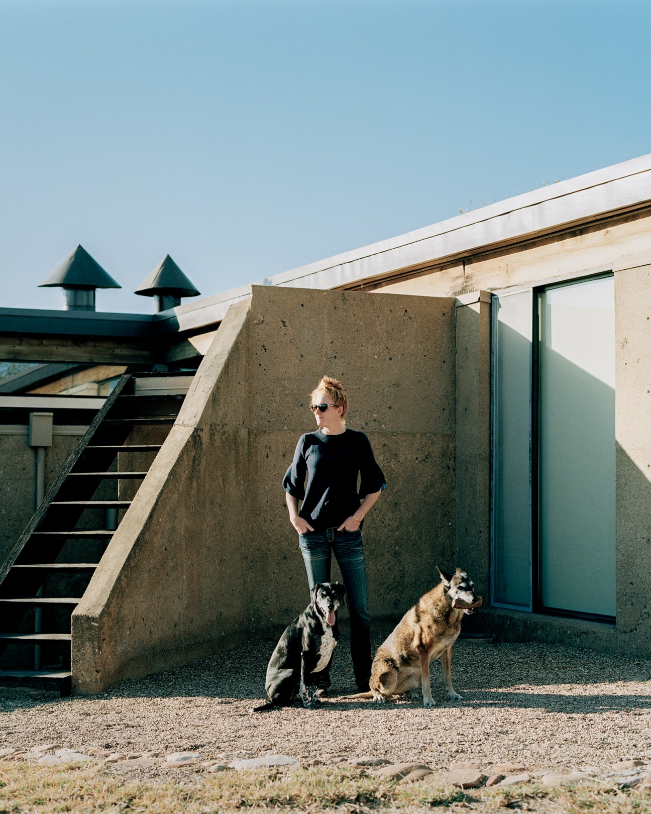 Diana Nijland standing with two dogs on concrete terrace of modernist desert house
