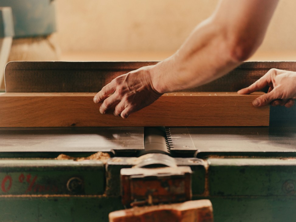 Hands guide wood through a machine tool, demonstrating furniture manufacturing craftsmanship.