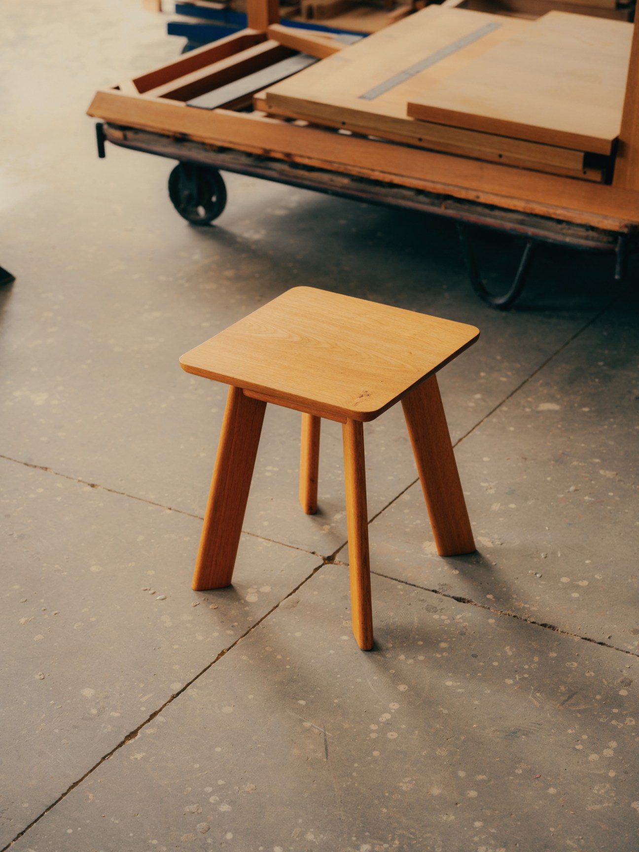 Wooden stool with rectangular top and four tapered legs in a workshop setting.