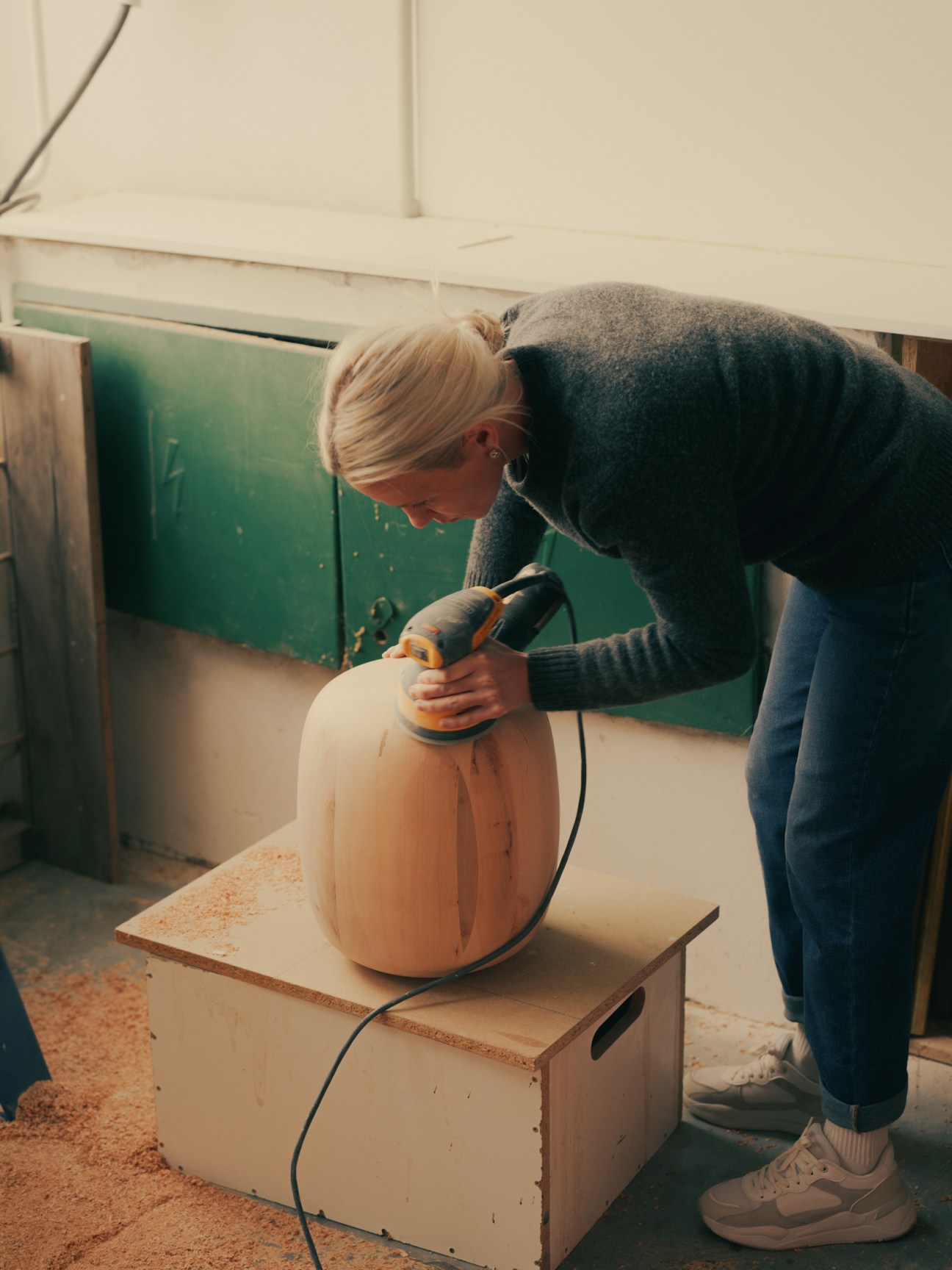 Person using an orbital sander on a wooden furniture piece in a workshop.
