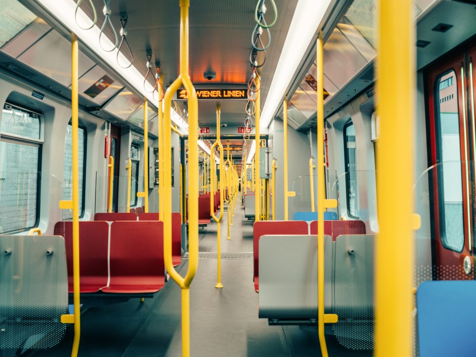Interior of Vienna's new X-Wagen train showing yellow railings, red and blue seating, and Wiener Linien branding.