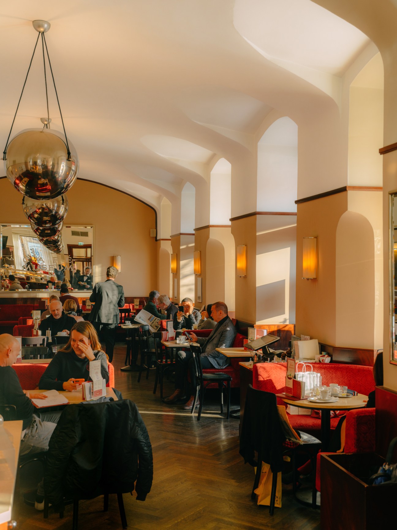 Historic Vienna cafe interior with vaulted ceilings, warm lighting, and patrons at red banquette seating