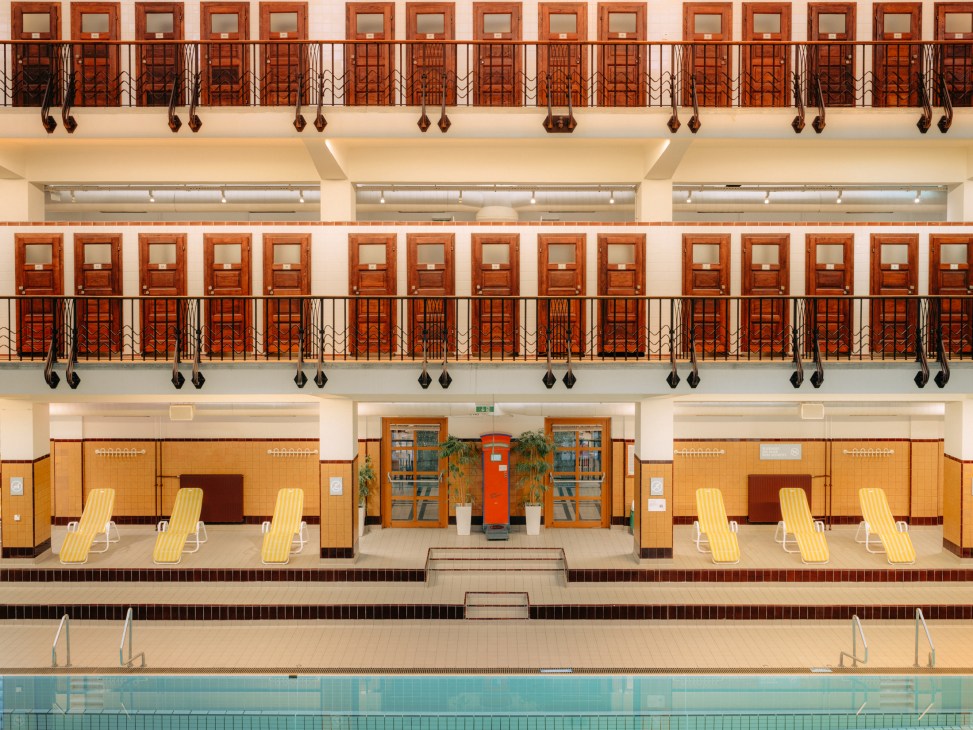 Interior view of a historic swimming pool with two levels of changing rooms and ornate railings