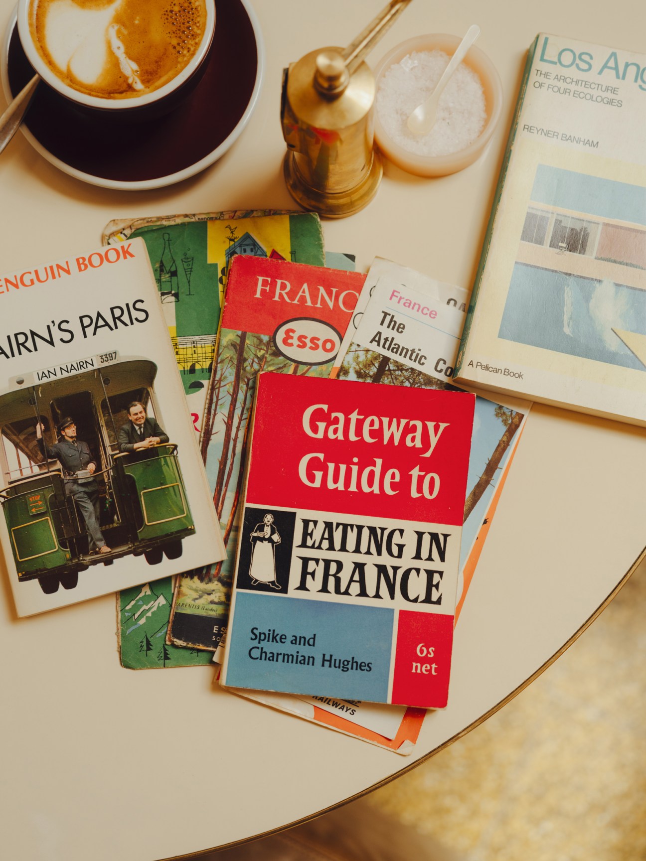 Collection of vintage travel guidebooks including Gateway Guide to Eating in France spread on table with coffee cup