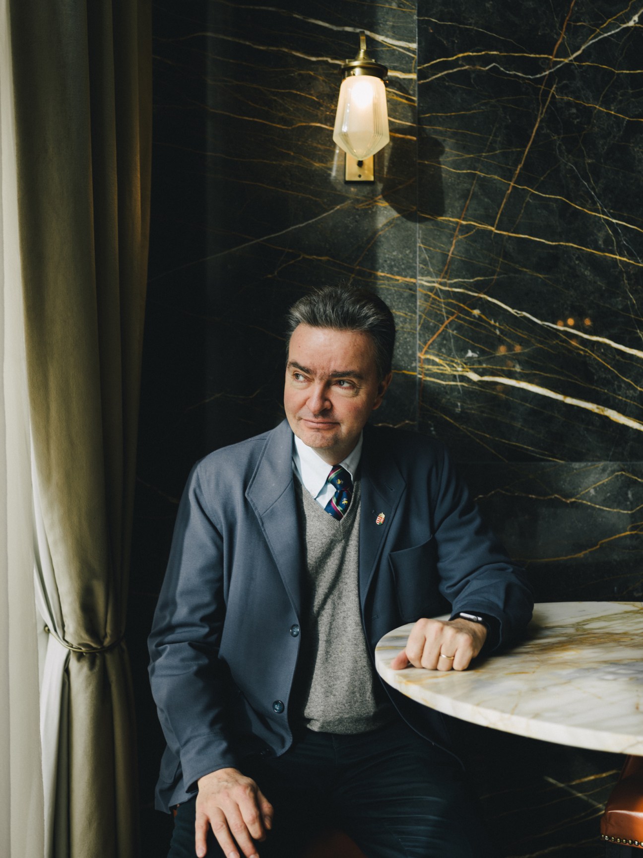 Georg von Habsburg sits at a marble table in an elegant interior with dark marble walls and pendant lighting