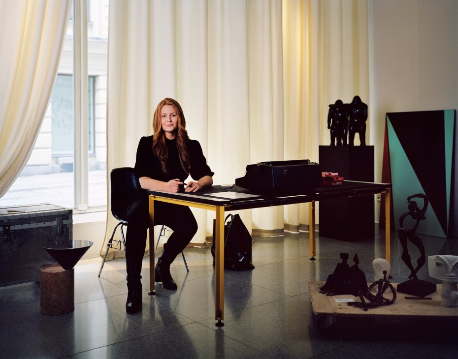 Louise Arén sitting at a desk in a dark-blue Eames DSS fibreglass chair at Bukowskis auction house