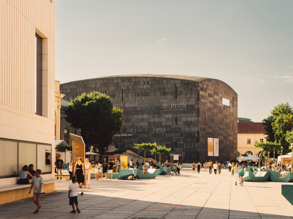 Modern circular museum building with dark stone facade and people gathered in plaza