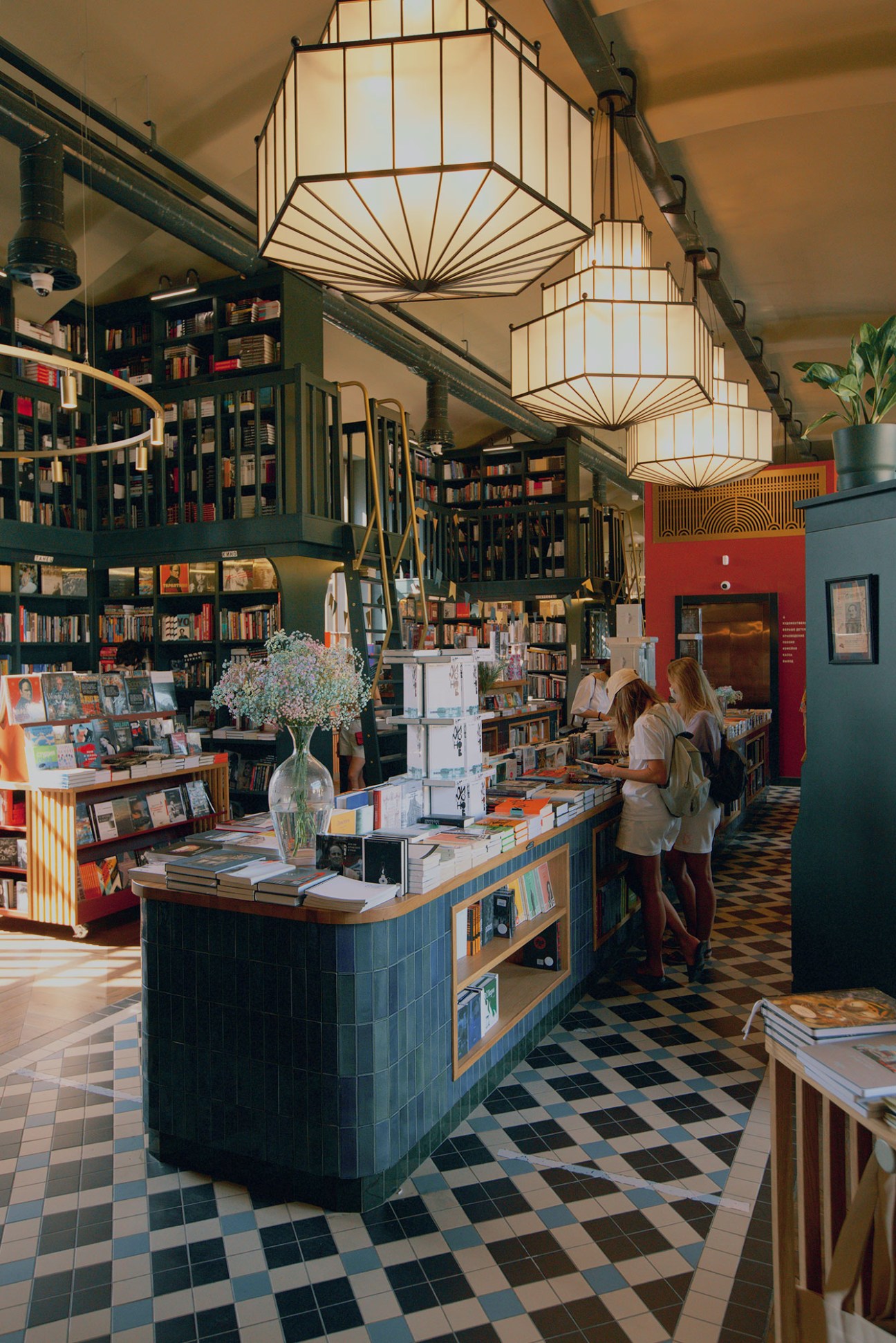Interior of Podpisnie Izdaniya bookshop with pendant lights, bookshelves, and customers browsing