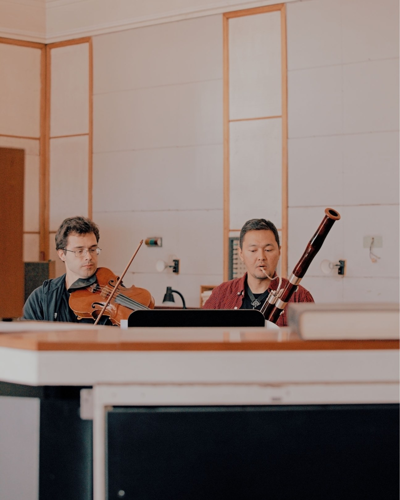 Two musicians practicing in Dom Radio rehearsal space, one playing violin and another with bassoon