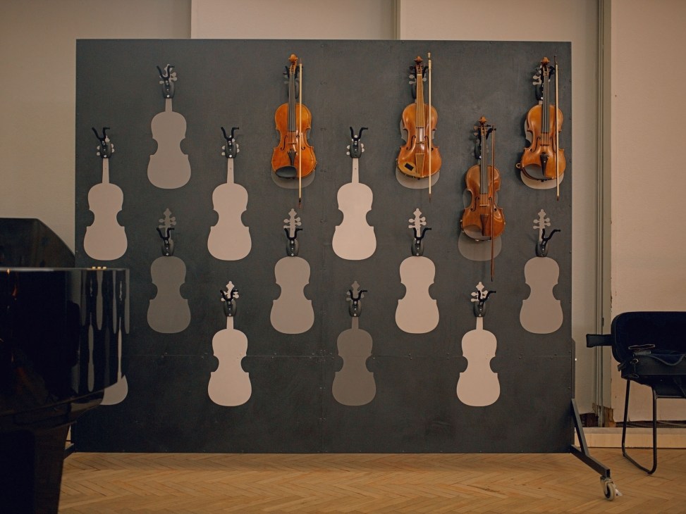 Wall display showing violin storage system with mounted pegs and violin silhouettes, several wooden violins hanging