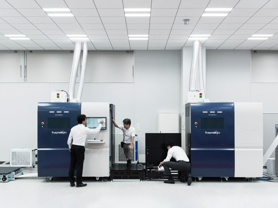Three technicians operating Truepress Jet printing machines in a clean white industrial facility
