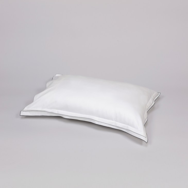 White pillow with grey piping detail against neutral background