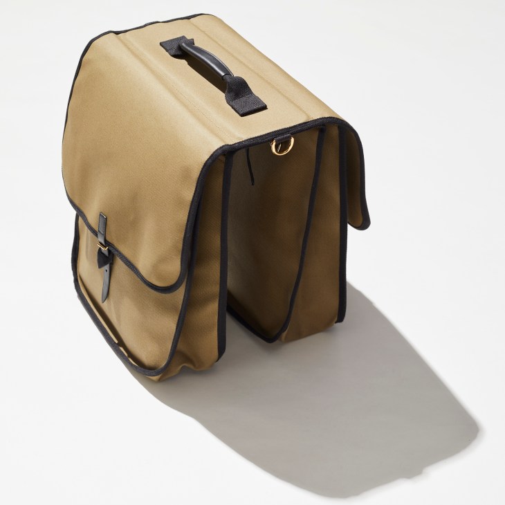 Tan canvas messenger bag with black trim and handle, showing dual compartments and adjustable shoulder strap photographed open to show interior compartments
