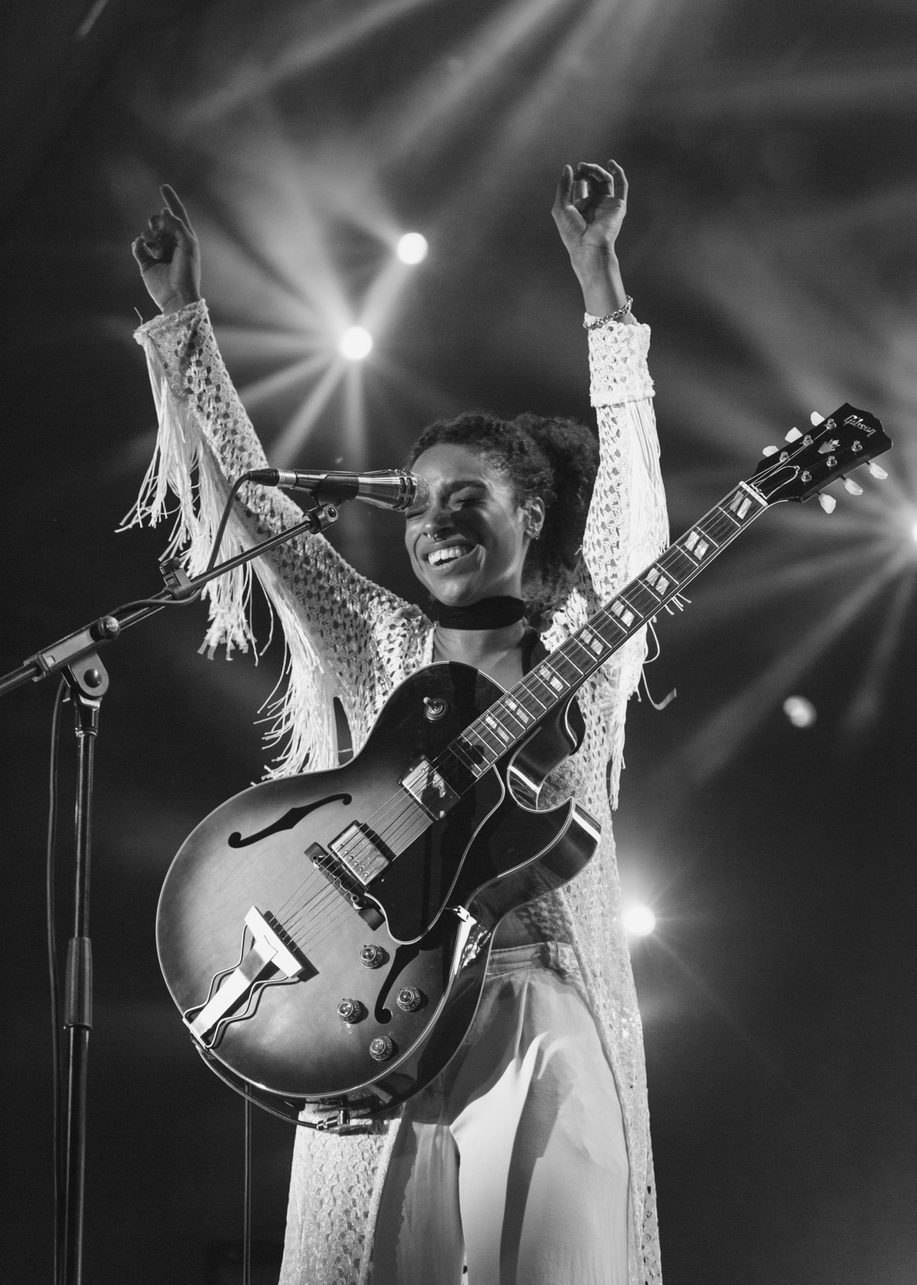 Musician performing on stage with guitar raised, arms up in celebration during live concert
