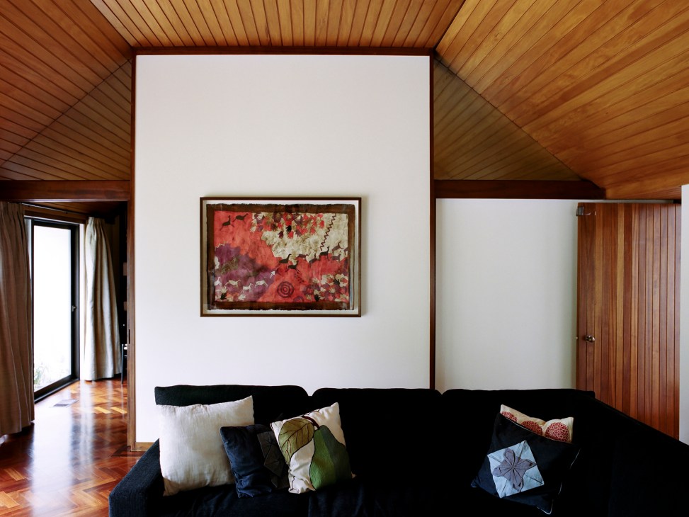 Interior room with dark sofa, colorful pillows, framed artwork on white wall, and wood-paneled slanted ceiling