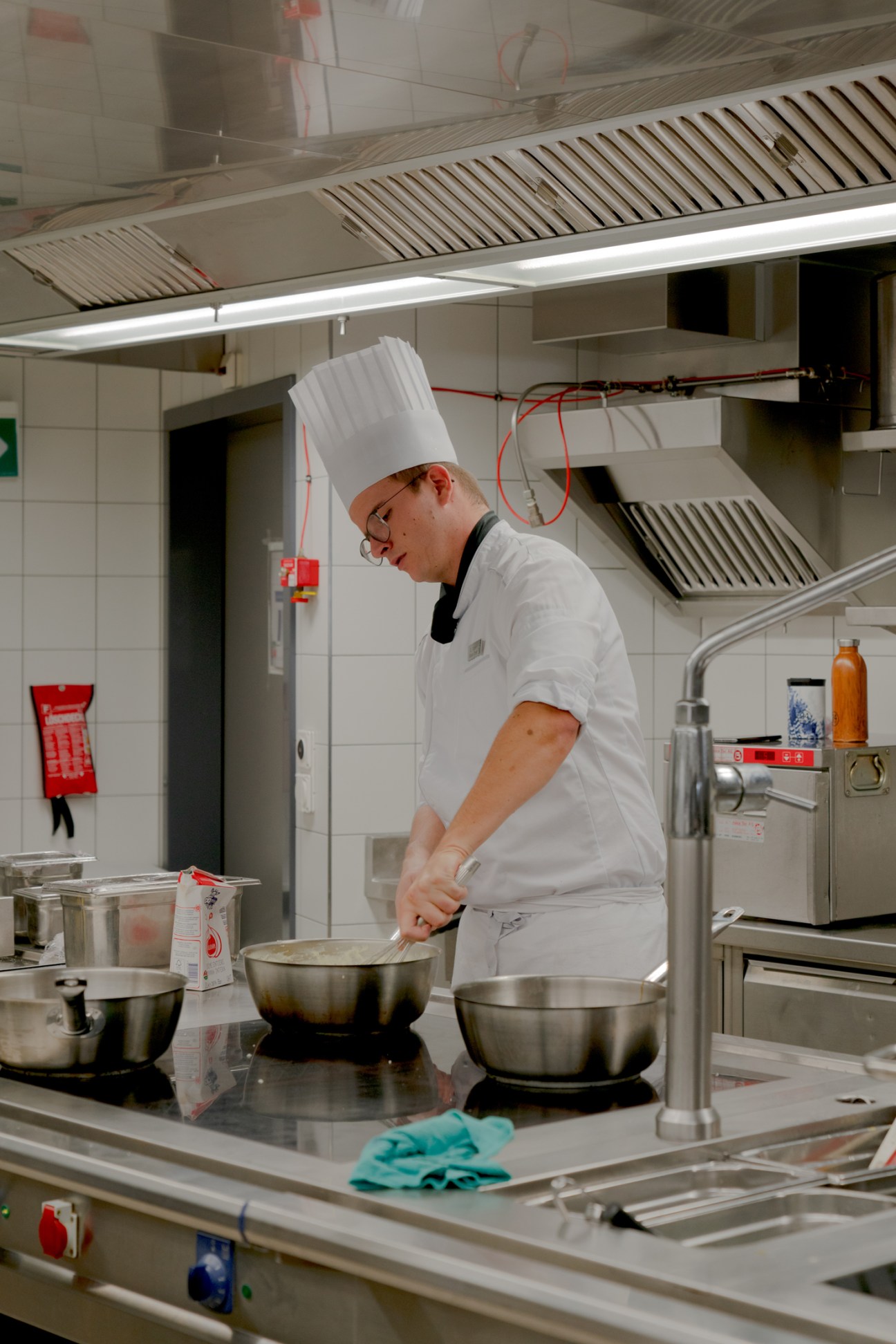 A chef in white uniform and tall hat cooking at stainless steel stove in professional kitchen