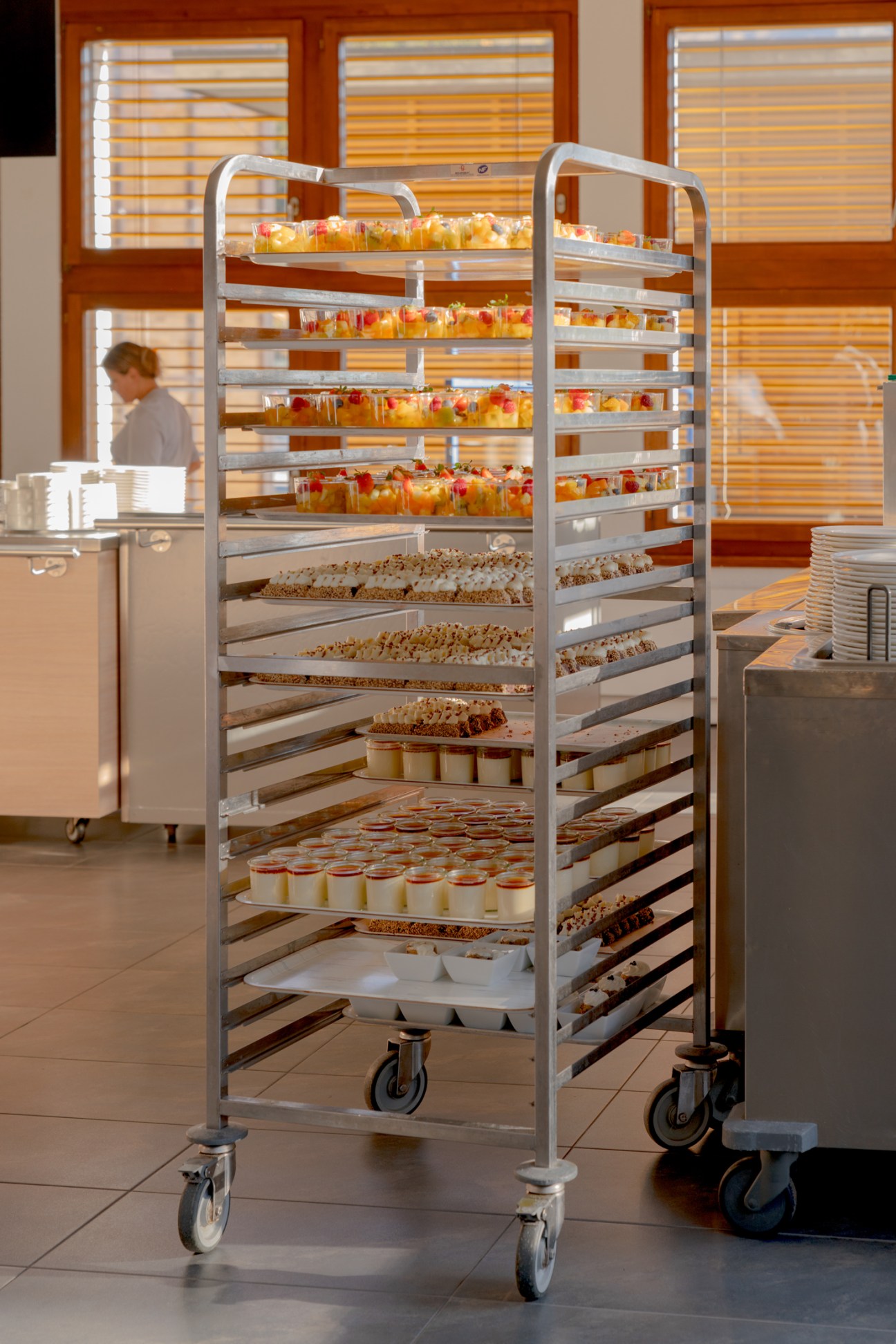 Mobile metal serving cart with multiple shelves displaying various desserts and pastries in a professional kitchen