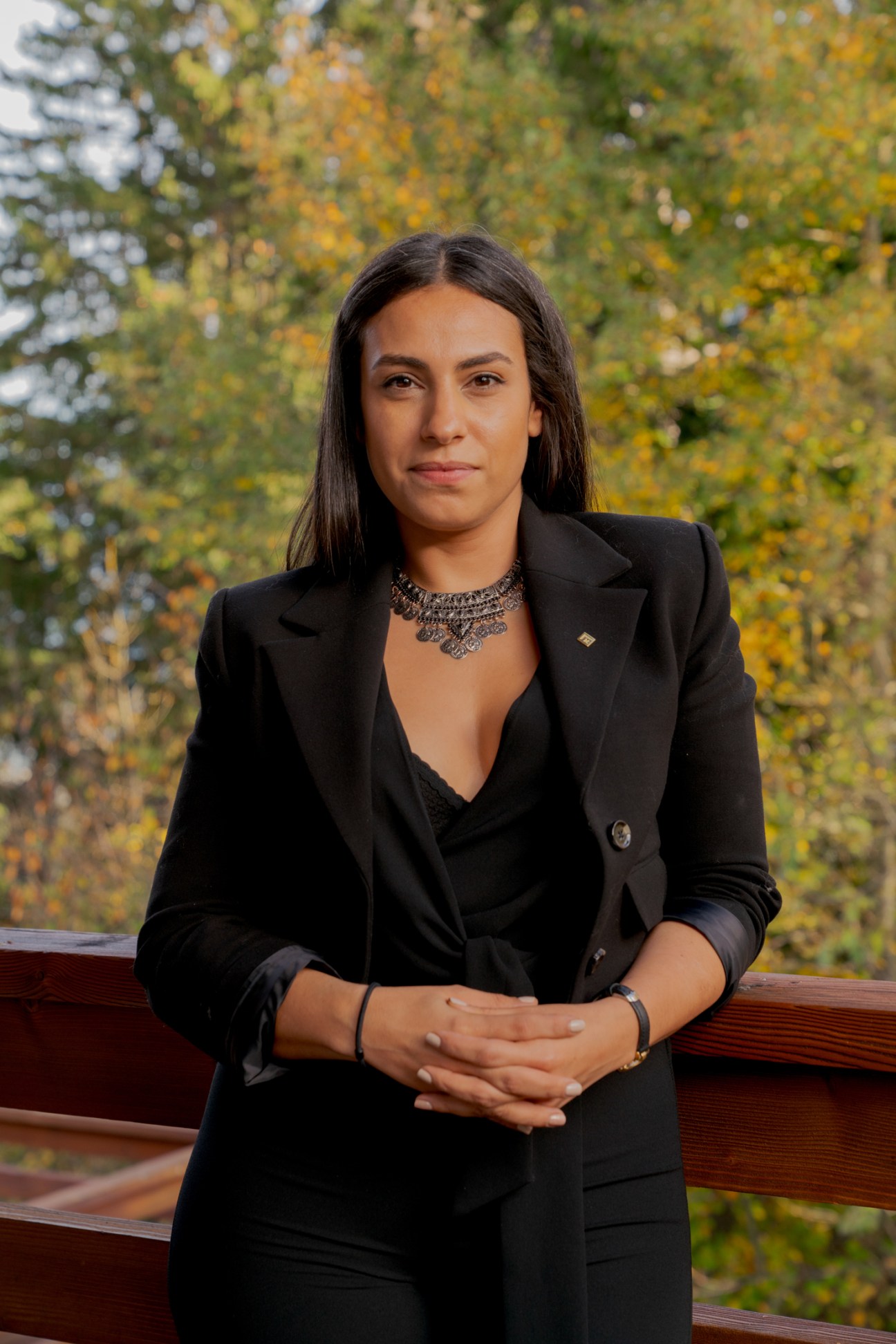 Salma Miss in professional black business attire seated outdoors with autumn foliage in background
