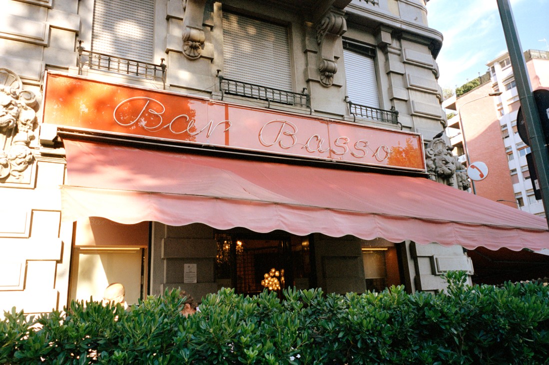 Bar Basso storefront with neon sign and pink awning on Milan street.