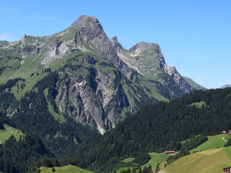Mountain landscape with winding road through green Alpine valley and traditional buildings