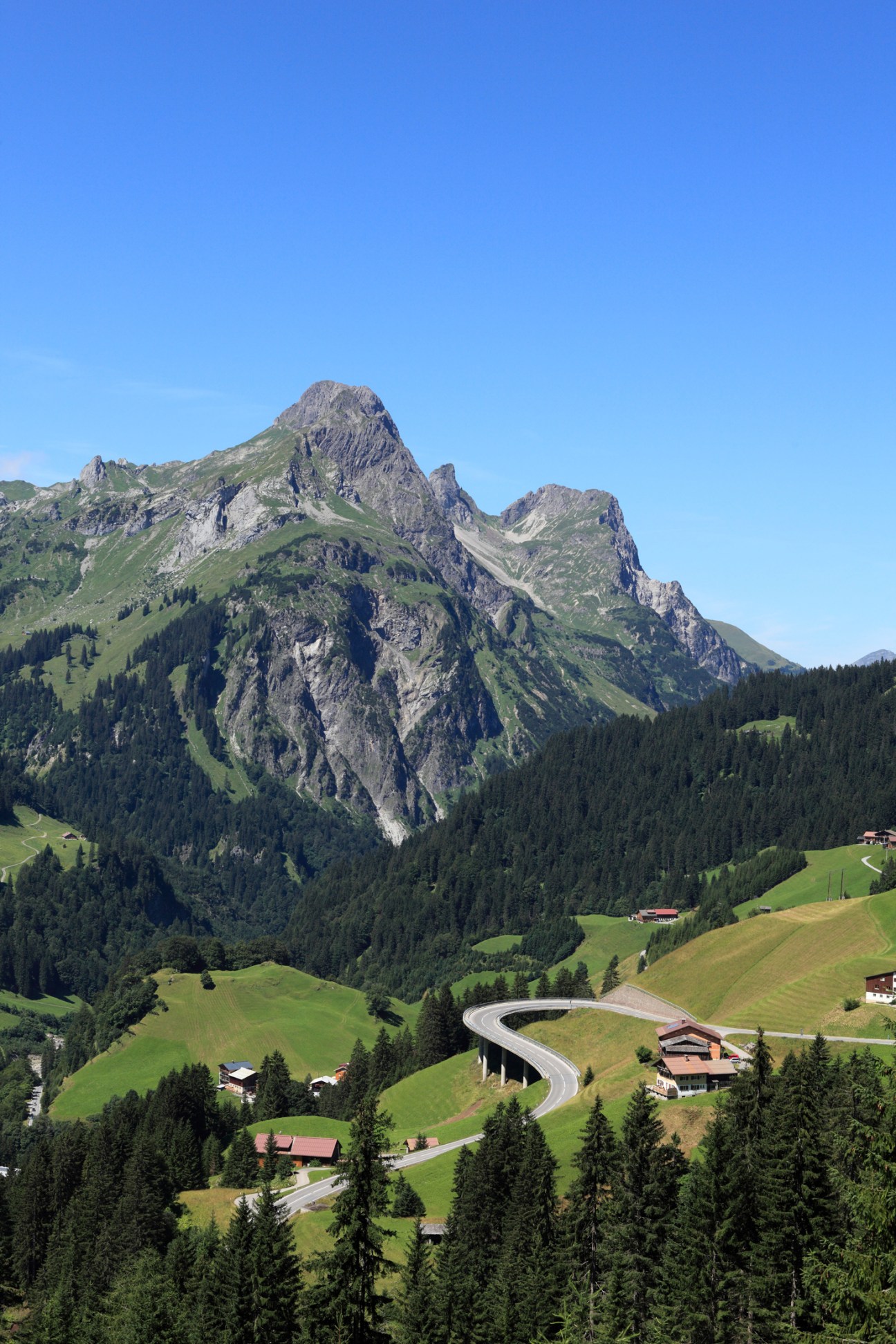 Mountain landscape with winding road through green Alpine valley and traditional buildings