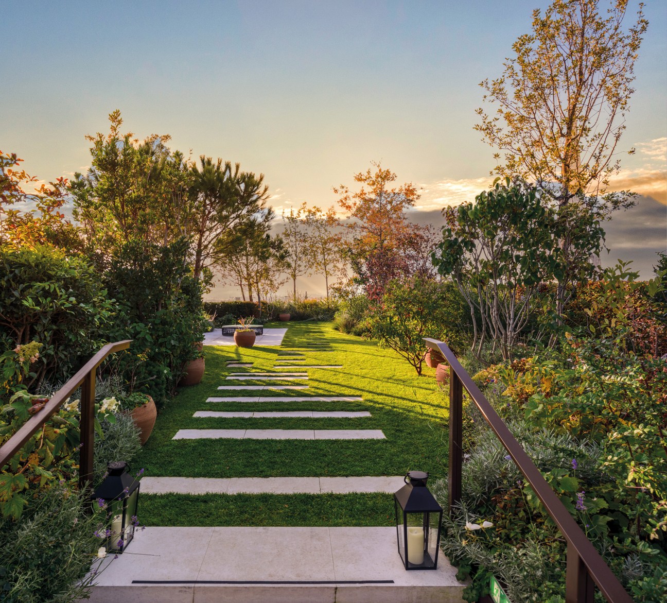 Garden terrace with stepping stone pathway through lawn, planters, and handrail at sunset