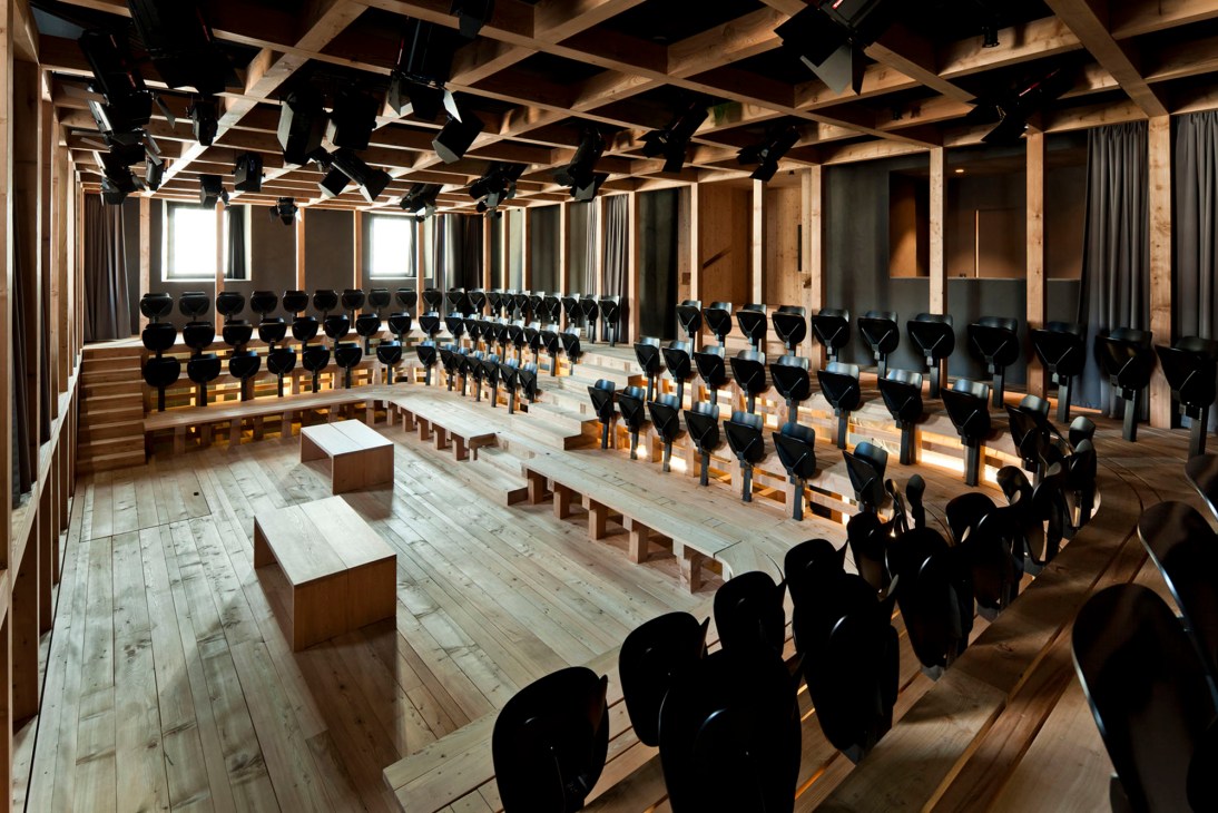Circular theater with tiered wooden seating surrounding central performance space, black chairs arranged in concentric rows