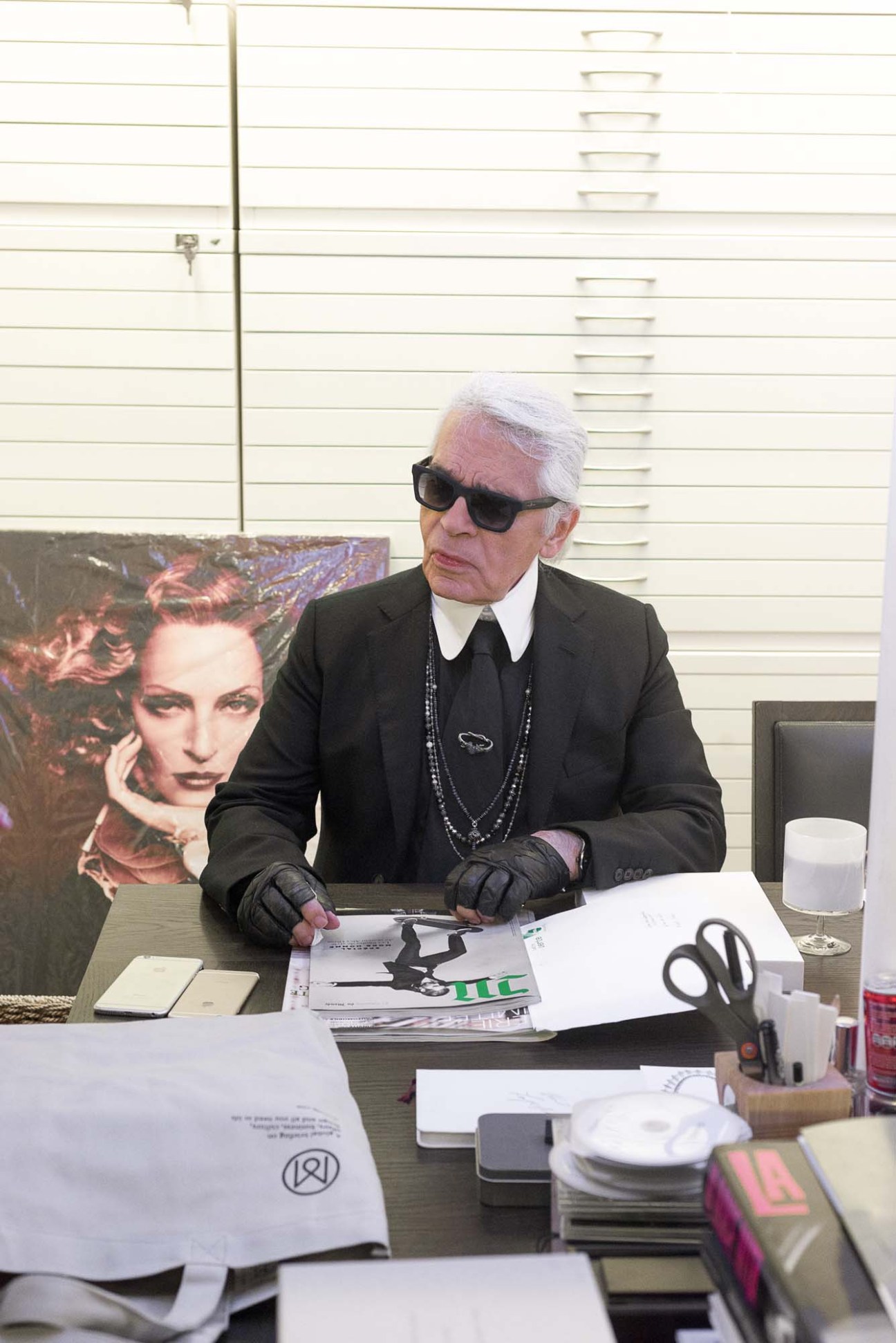 Karl Lagerfeld in dark sunglasses and black suit sitting at desk during radio interview