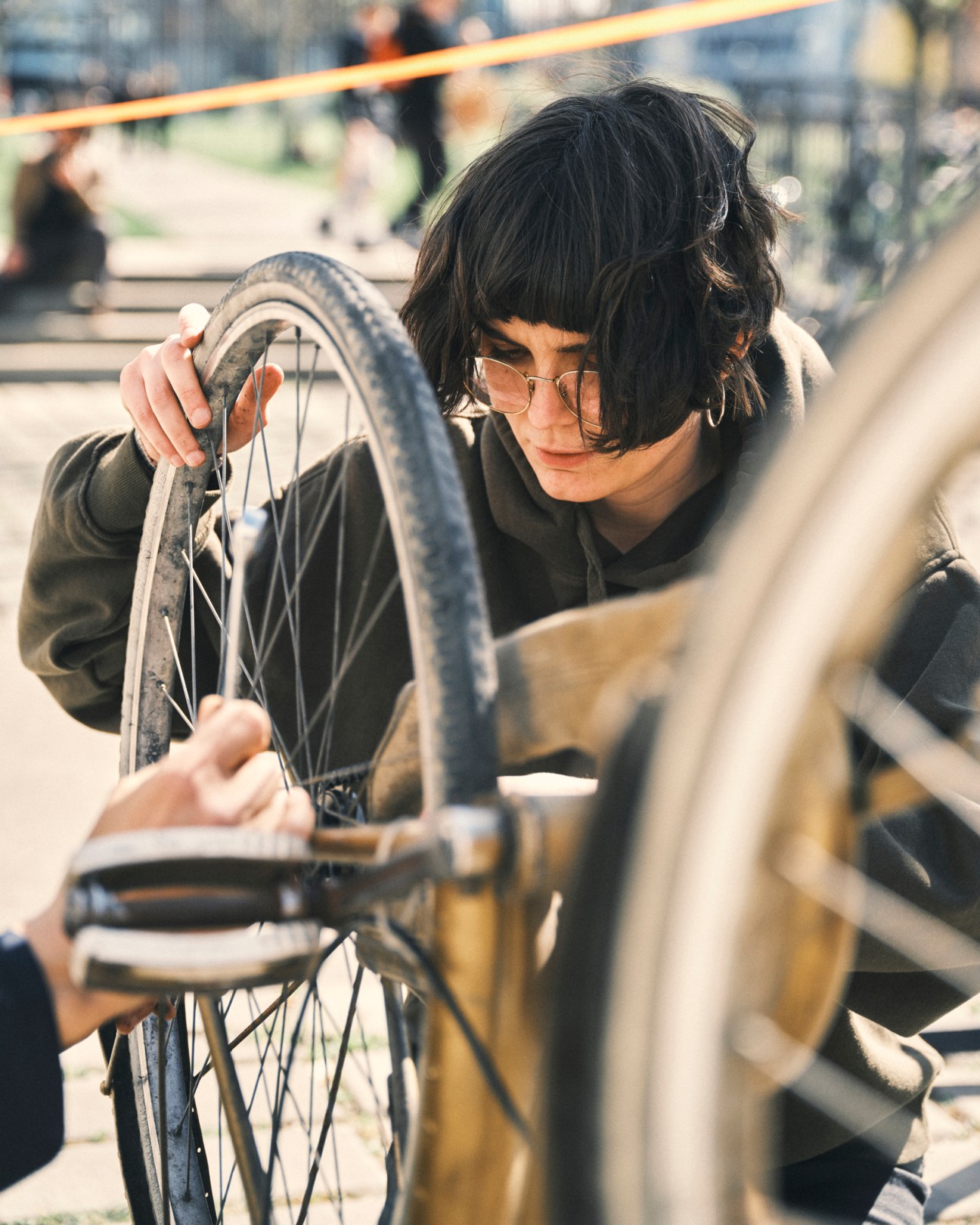 Person with dark hair and sunglasses working on bicycle wheel repair at workshop station