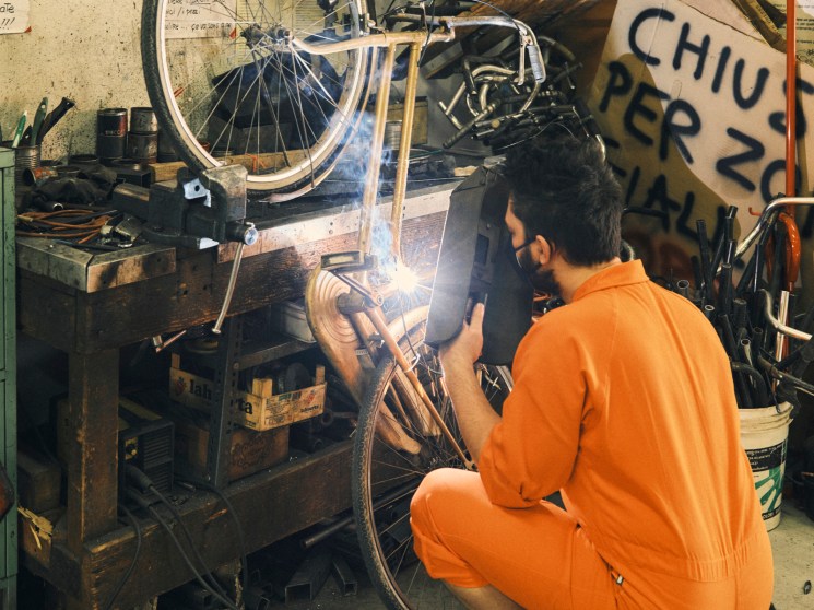 Rocco Guarna in an orange boiler suit working with soldering equipment in the workshop