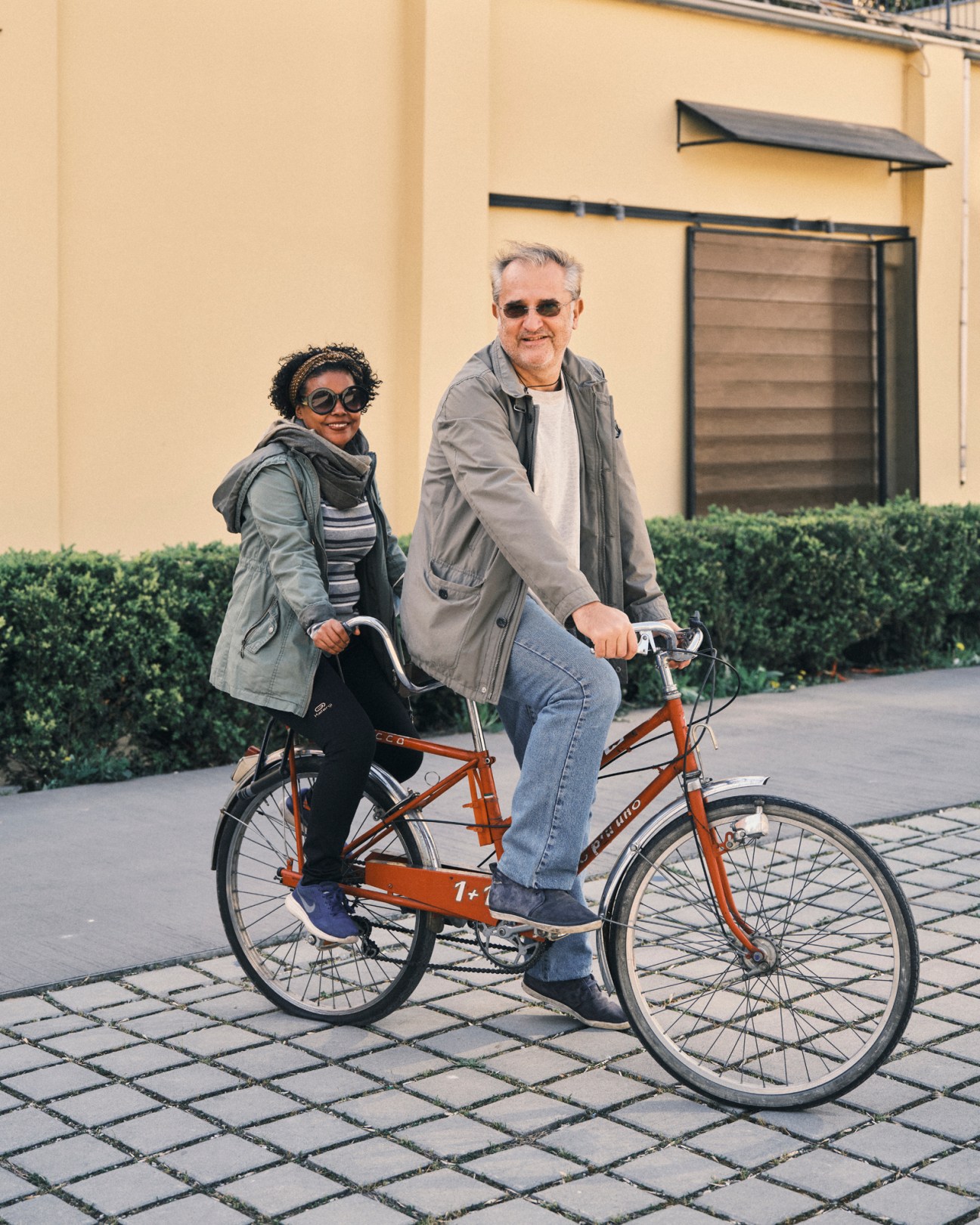 Man and woman posing with vintage red tandem bicycle on cobblestone street