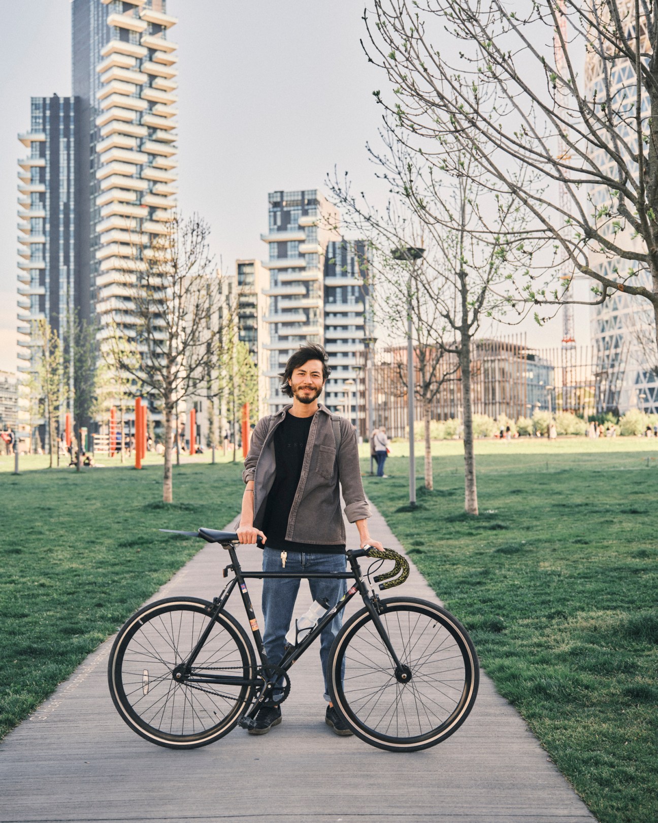 Loris Garda standing with his bicycle in an urban park setting with modern buildings in the background