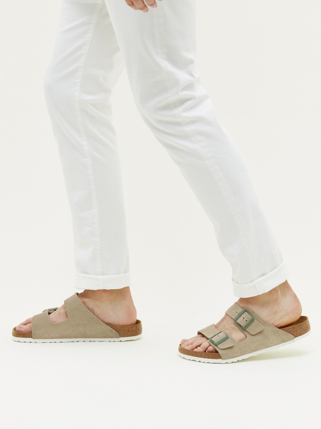 Person wearing taupe suede Birkenstock Arizona sandals with white wide-leg pants