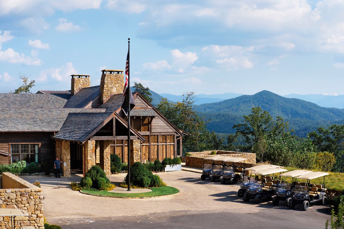 Stone cottage with American flag at Blackberry Mountain overlooking forested Great Smoky Mountains under cloudy blue sky.