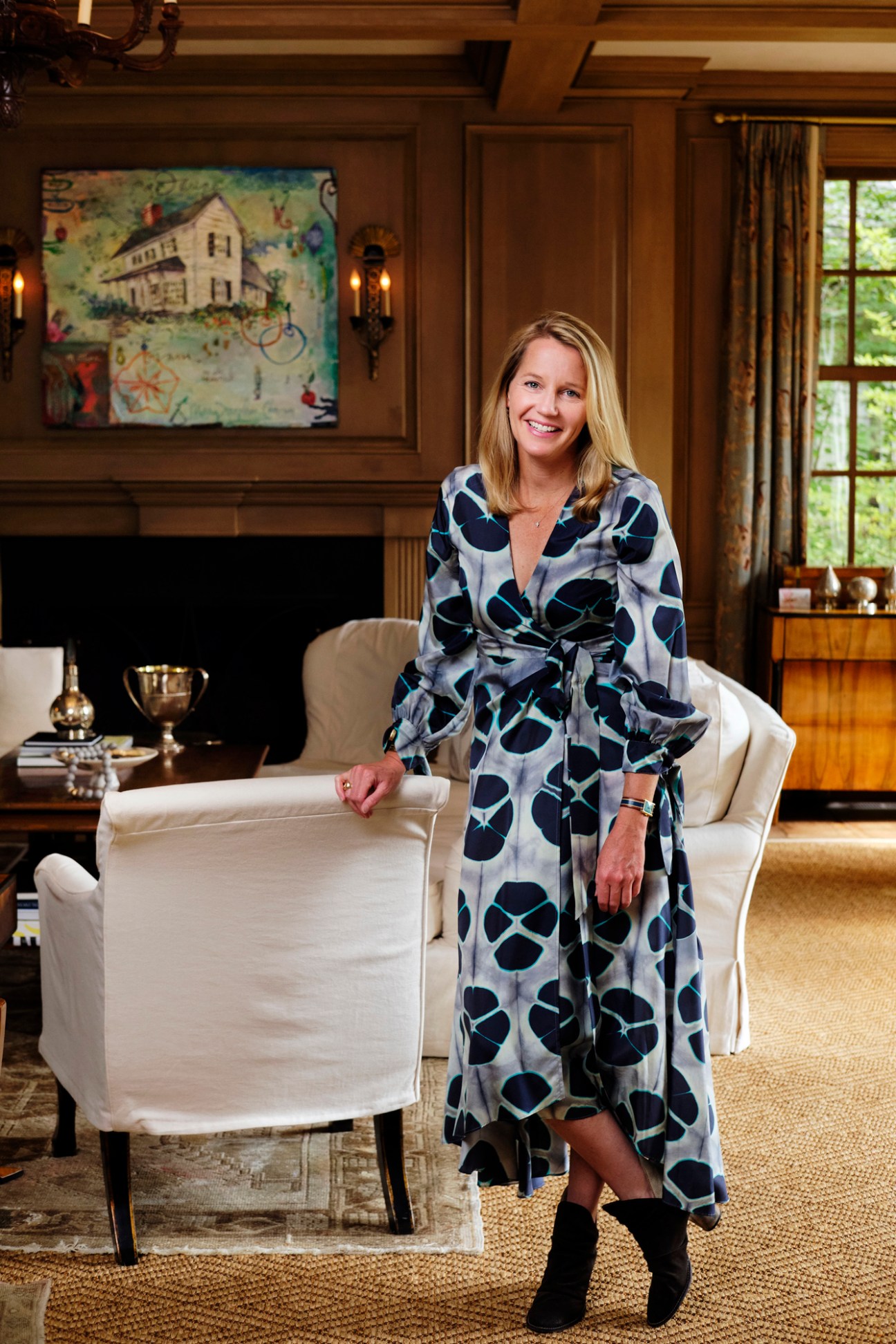 Mary Celeste Bealle stands in an elegant living room with a fireplace and patterned artwork.
