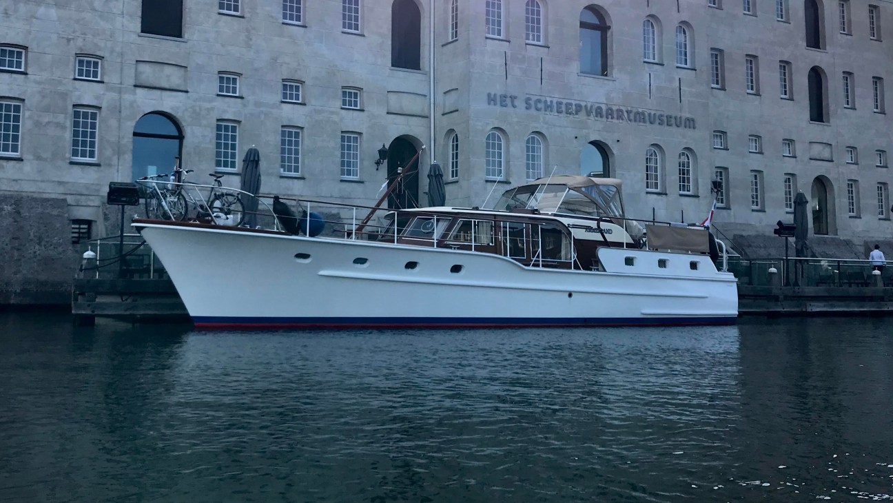 A white classic yacht moored in front of the Het Scheepvaartmuseum building in Amsterdam