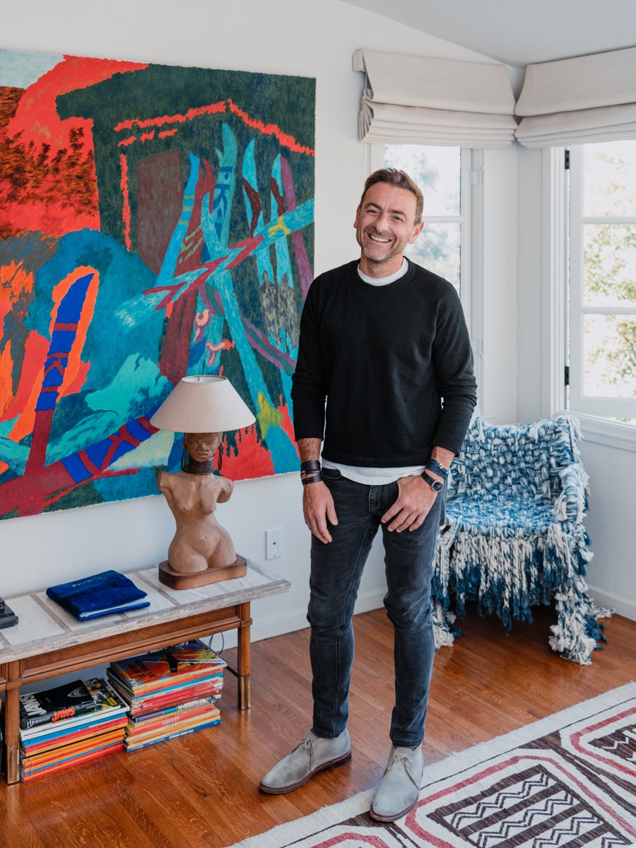 Man standing in bright living room with large colorful abstract painting, patterned throw, and side table with lamp