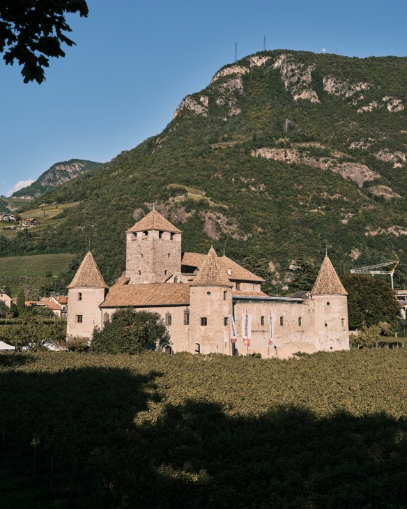 Medieval castle with multiple towers and crenellated walls set against forested mountains in Bolzano, Italy.