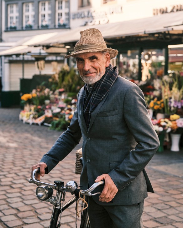 Man in straw hat and blue blazer with bicycle on Bolzano street with flower market.