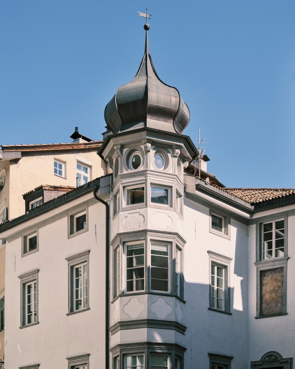 Bolzano building with distinctive onion-domed tower and cream-colored facade against blue sky.