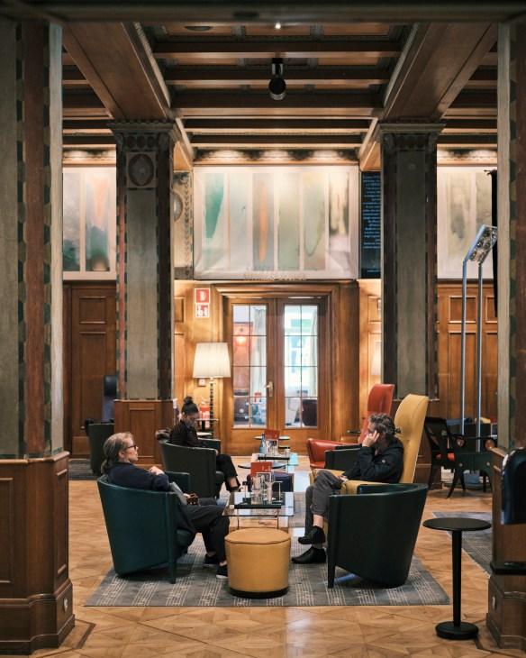 Interior of a modern hotel lobby with wooden columns, contemporary seating, and guests conversing.