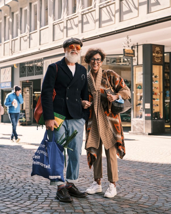 Two people walking on a cobblestone street in Bolzano with historic buildings and storefronts in the background.