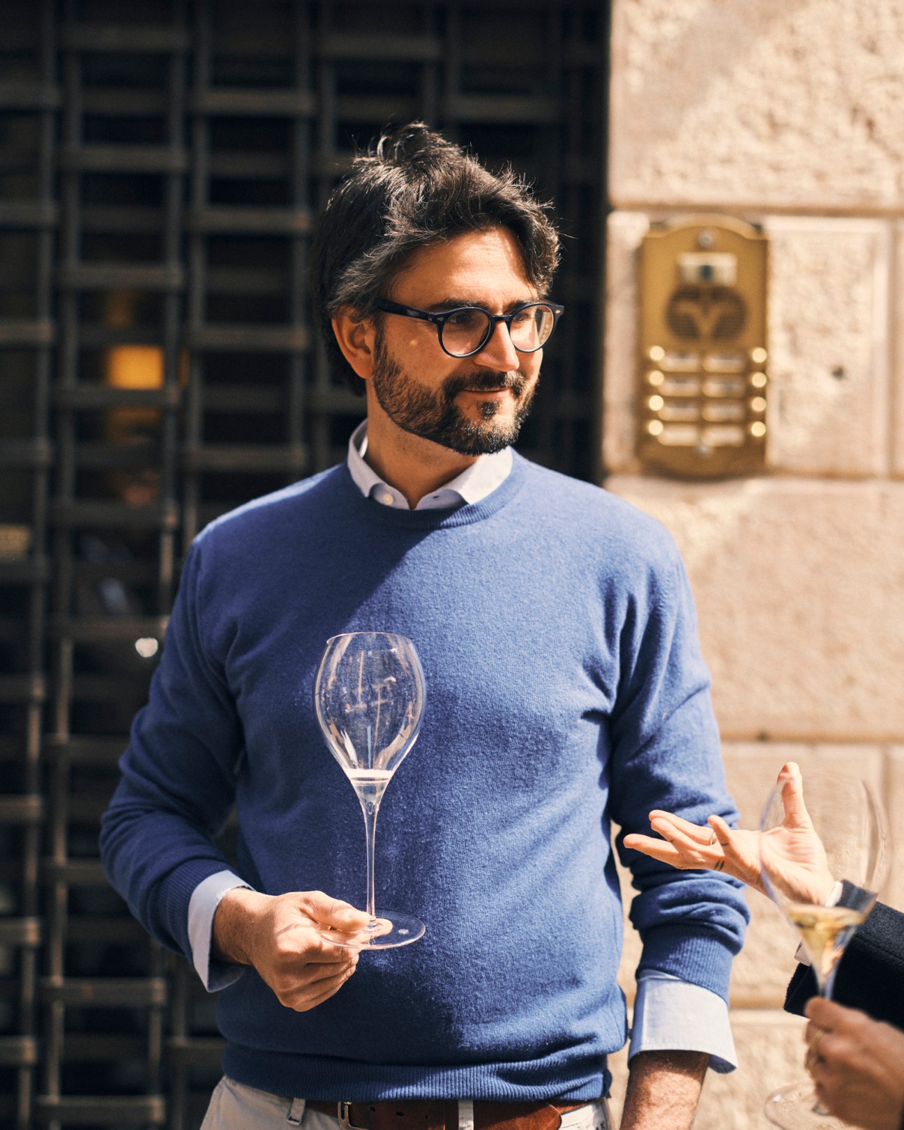 Wine-maker Giovanni Éderle holding a wine glass outdoors, wearing glasses and a blue sweater