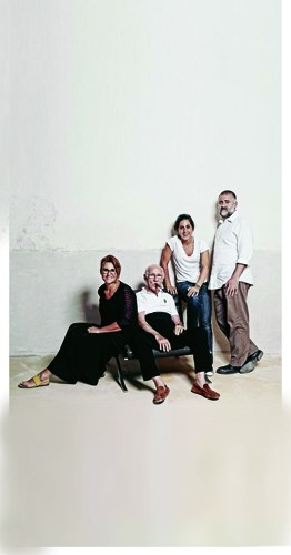 Group of four people posing against a white wall in casual business attire.