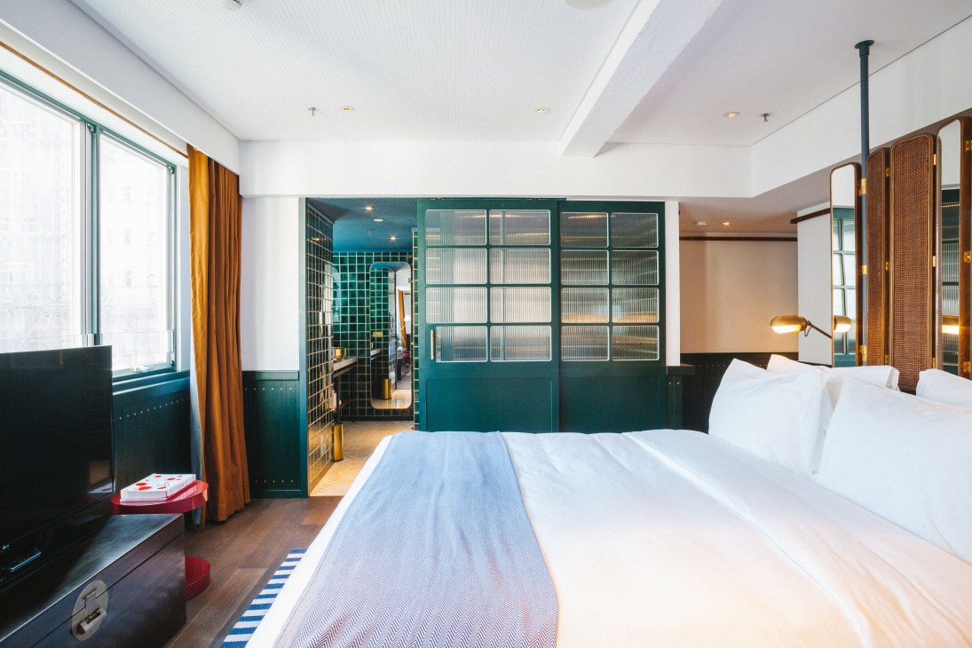 Modern hotel bedroom with teal accent wall, white bedding, and contemporary furnishings at The Fleming Hotel.