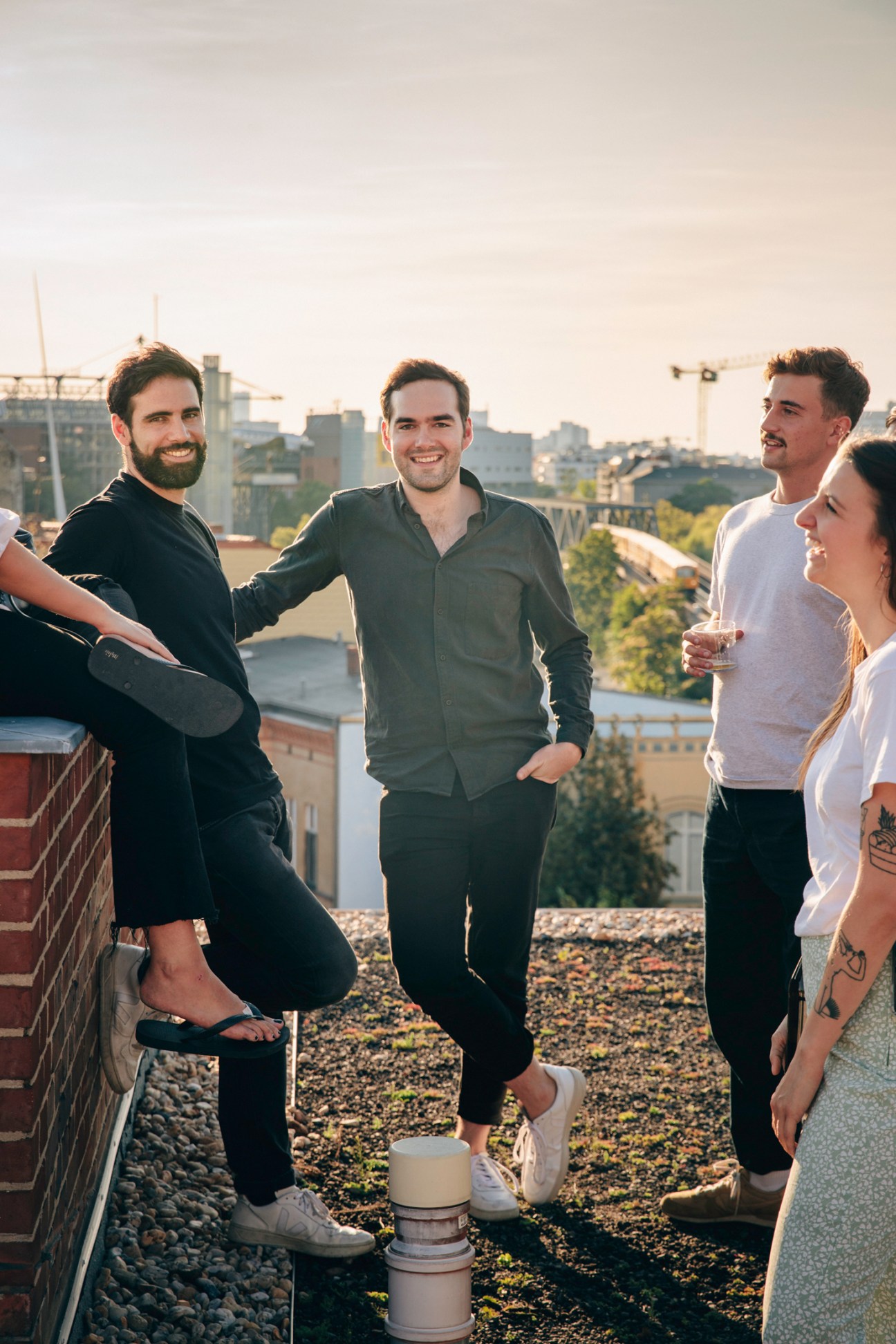 Four people smiling on a rooftop with Berlin cityscape and construction cranes visible in the background.