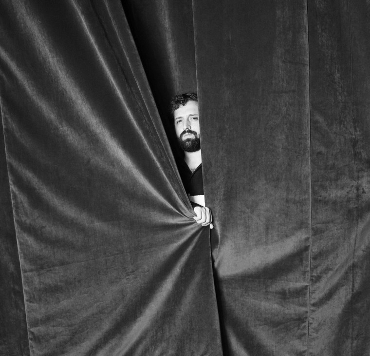 Gregório Duvivier, Brazilian comedian and satirical news presenter, peering through dark curtains