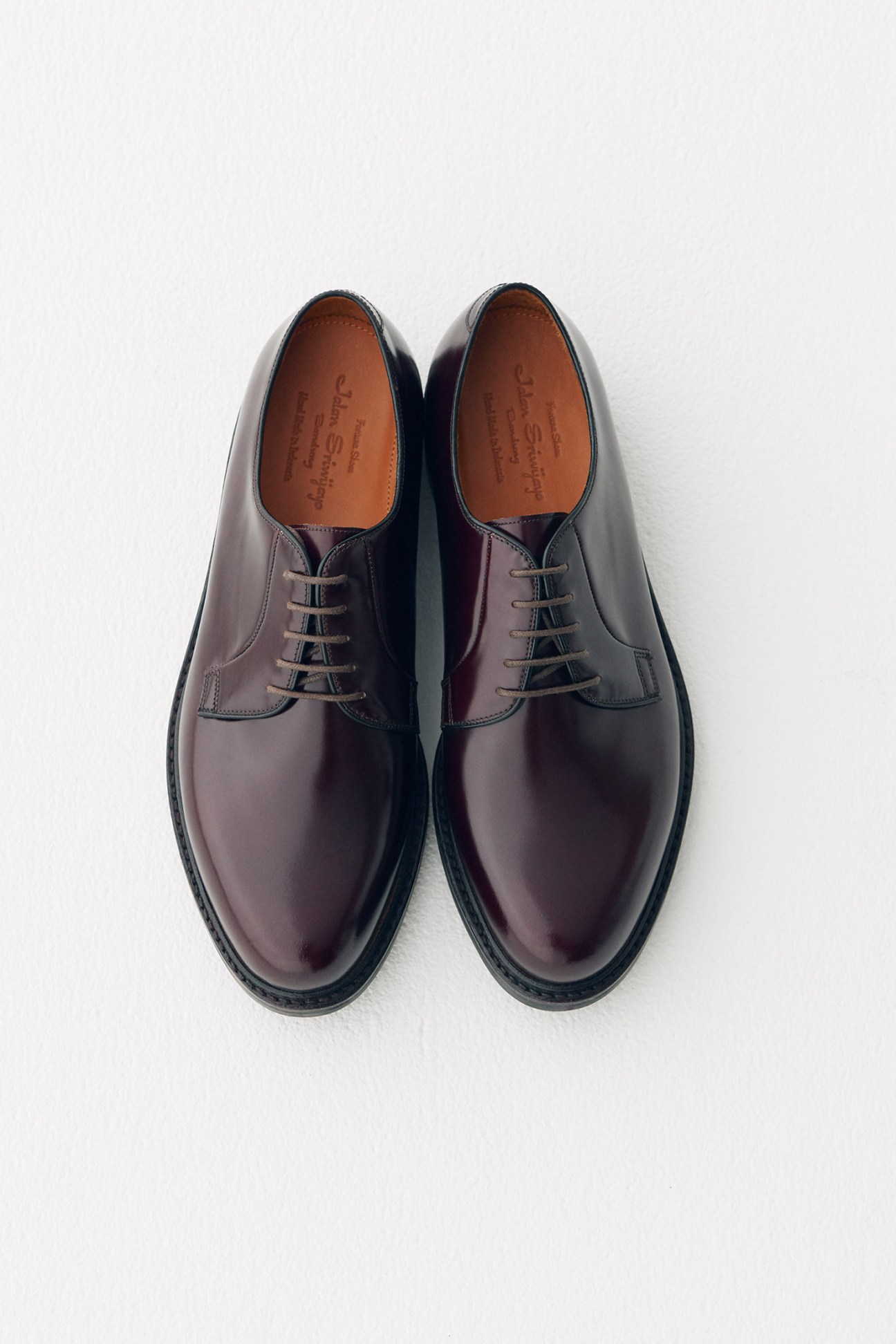 Pair of burgundy leather oxford shoes with tan insoles, displayed flat on white background.